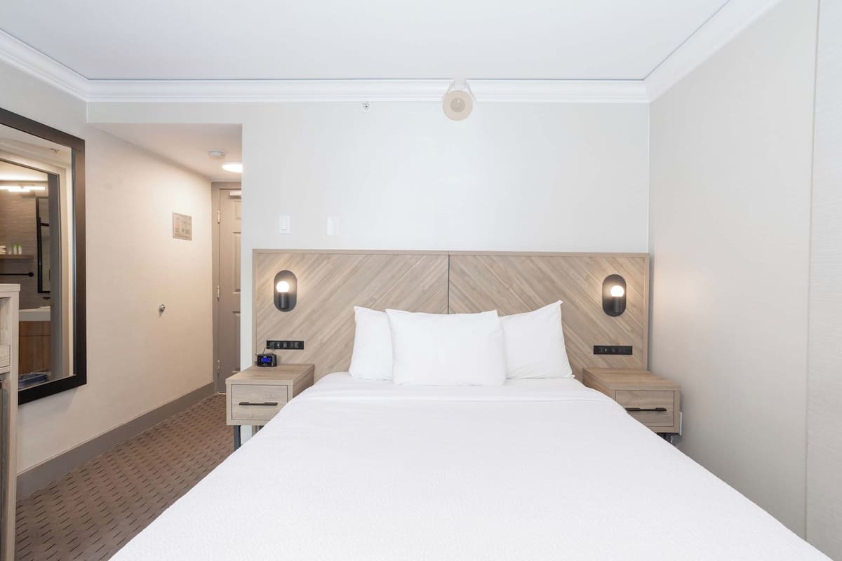 Een hotelkamer met een groot bed, twee nachtkastjes, een spiegel en een houten hoofdbord.