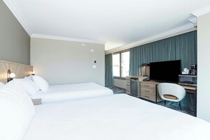 Habitación de hotel con dos camas, un escritorio, un televisor de pantalla plana, una silla y una kitchenette pequeña.