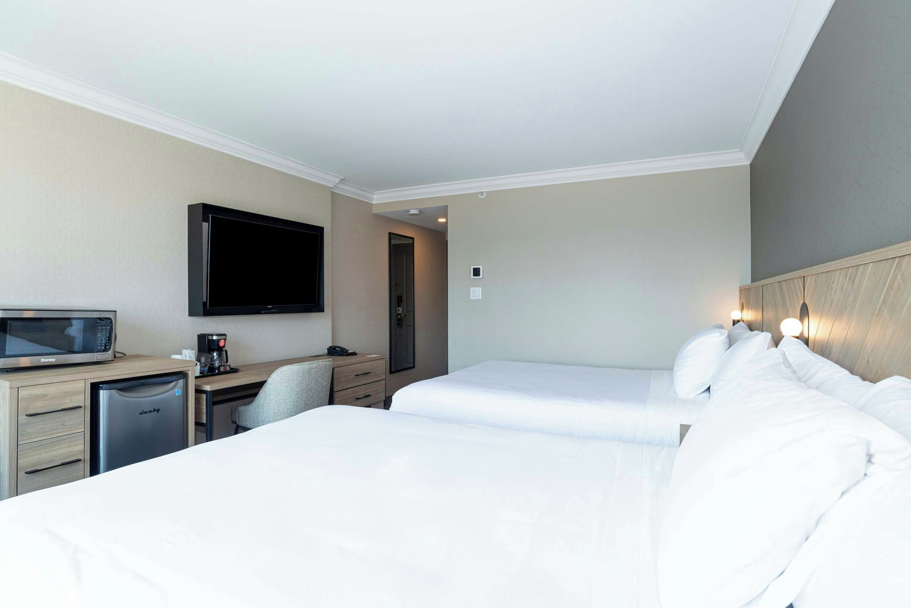 Una habitación de hotel con dos camas, un escritorio con microondas, cafetera y televisor en la pared.