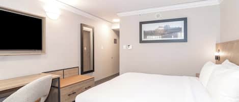 Una habitación de hotel con una cama, un escritorio, una silla, un televisor y un cuadro en la pared.