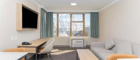 Una habitación de hotel moderna con escritorio, sofá y un amplio ventanal con vista a la ciudad.