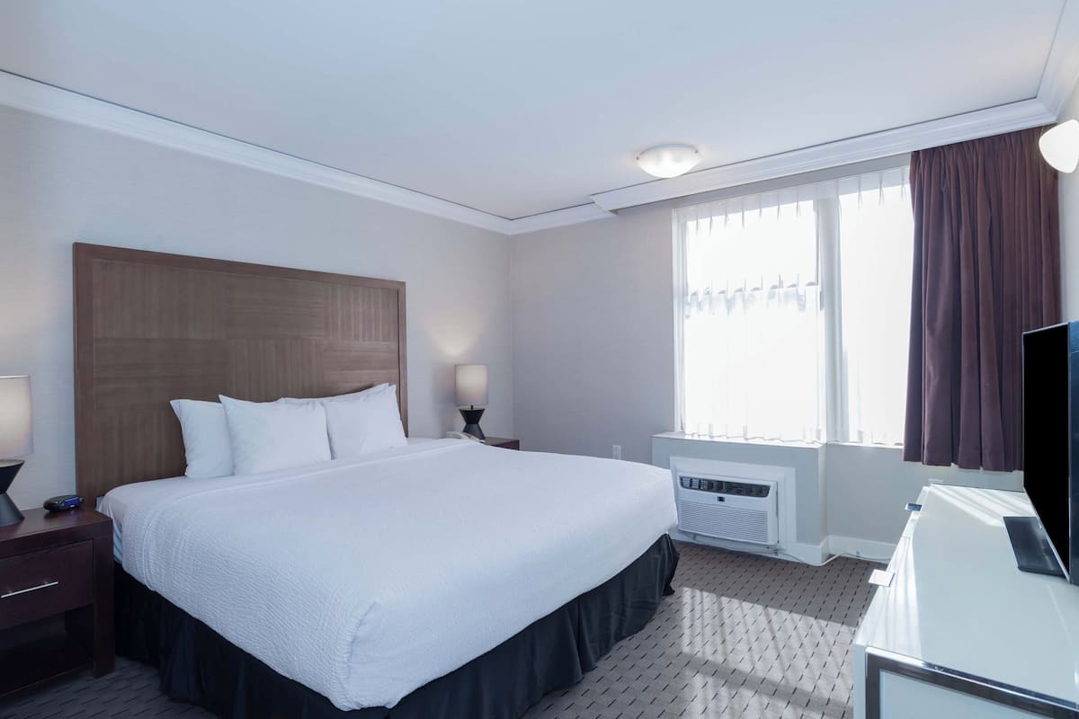 Een hotelkamer met een groot bed, nachtlampjes, een televisie en een raam met gordijnen.