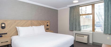 Une chambre d’hôtel comprenant un lit, une table de chevet, une lampe fixée au mur, une fenêtre avec des rideaux et un radiateur.