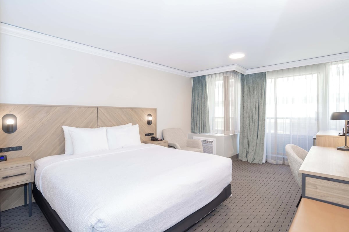 Een hotelkamer met een groot bed, een bureau, een stoel en een raam met gordijnen.