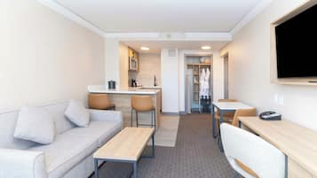A compact hotel room with a kitchenette, a sofa, a dining table, and a TV.