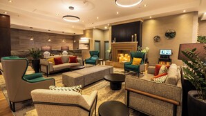 Un moderno vestíbulo de hotel con un conjunto de sofás, sillones, una chimenea y una televisión.