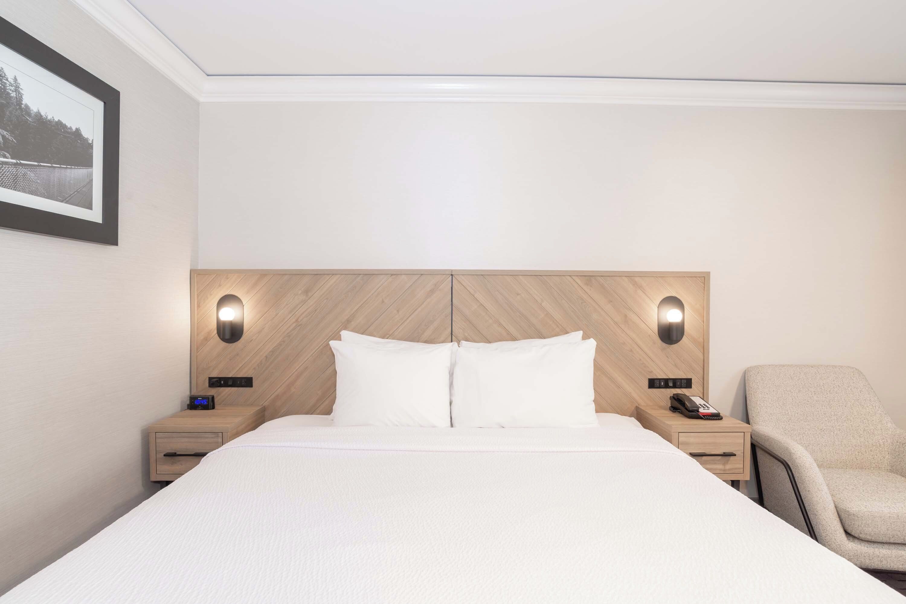 Une chambre d’hôtel avec un grand lit, deux tables de chevet, une chaise et une tête de lit dotée d’un éclairage intégré.