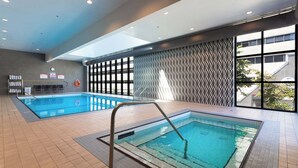 Una piscina interior con suelo de baldosas, una escalera metálica y una pared con un diseño geométrico.