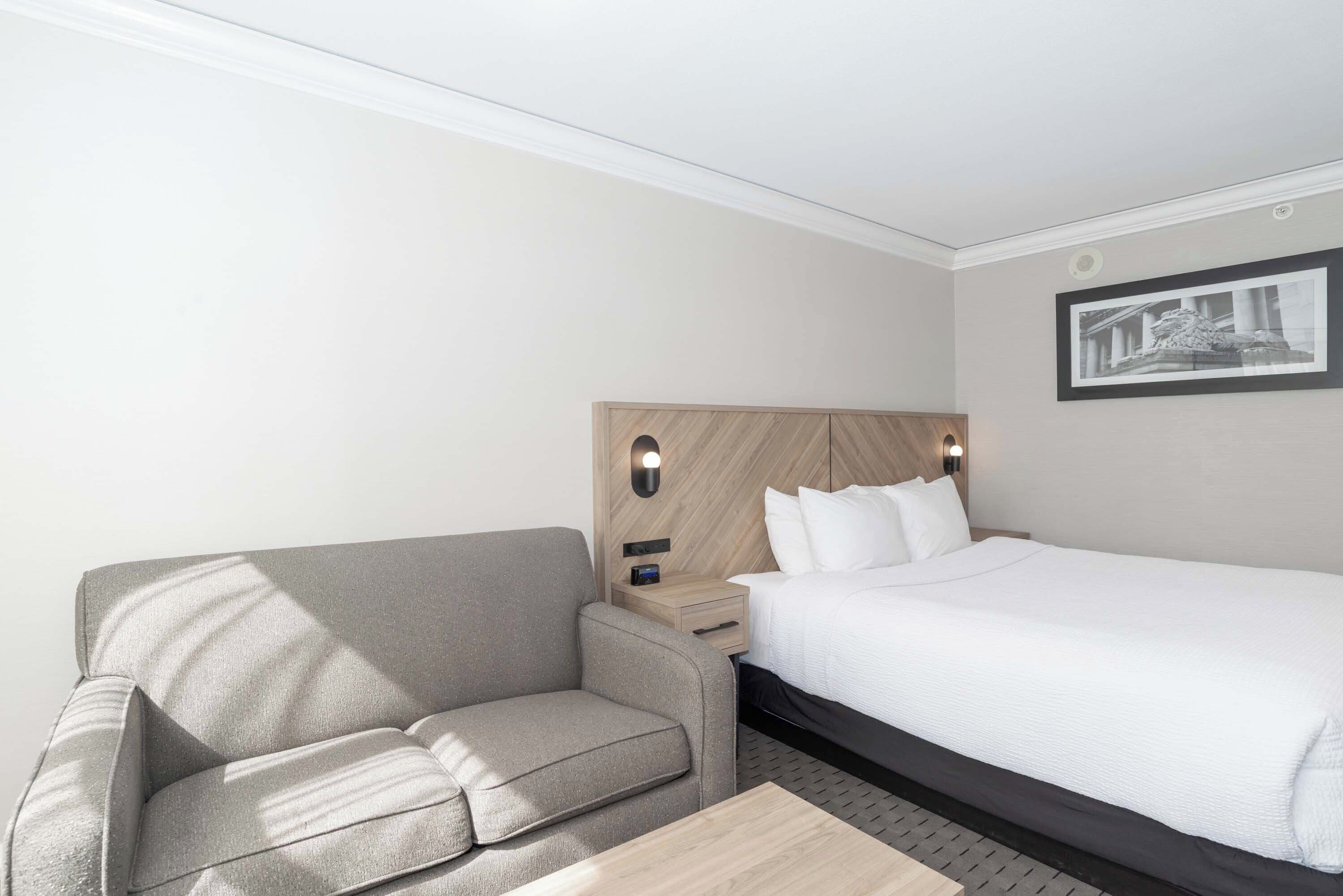 A hotel room with a bed, a sofa, a nightstand, and a wall-mounted picture.