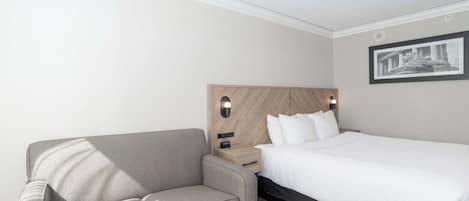 Una habitación de hotel con cama, sofá, mesita de noche y un cuadro colgado en la pared.