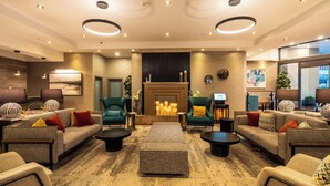 Un moderno vestíbulo de hotel con sofás, sillones, una chimenea y un ventanal grande.