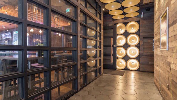 Un interior moderno con pisos hexagonales, divisiones de vidrio y una pared de madera con lámparas circulares.