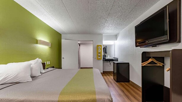 Ein Hotelzimmer mit Bett, Fernseher, einer kleinen Küchenzeile und einem Kleiderständer.