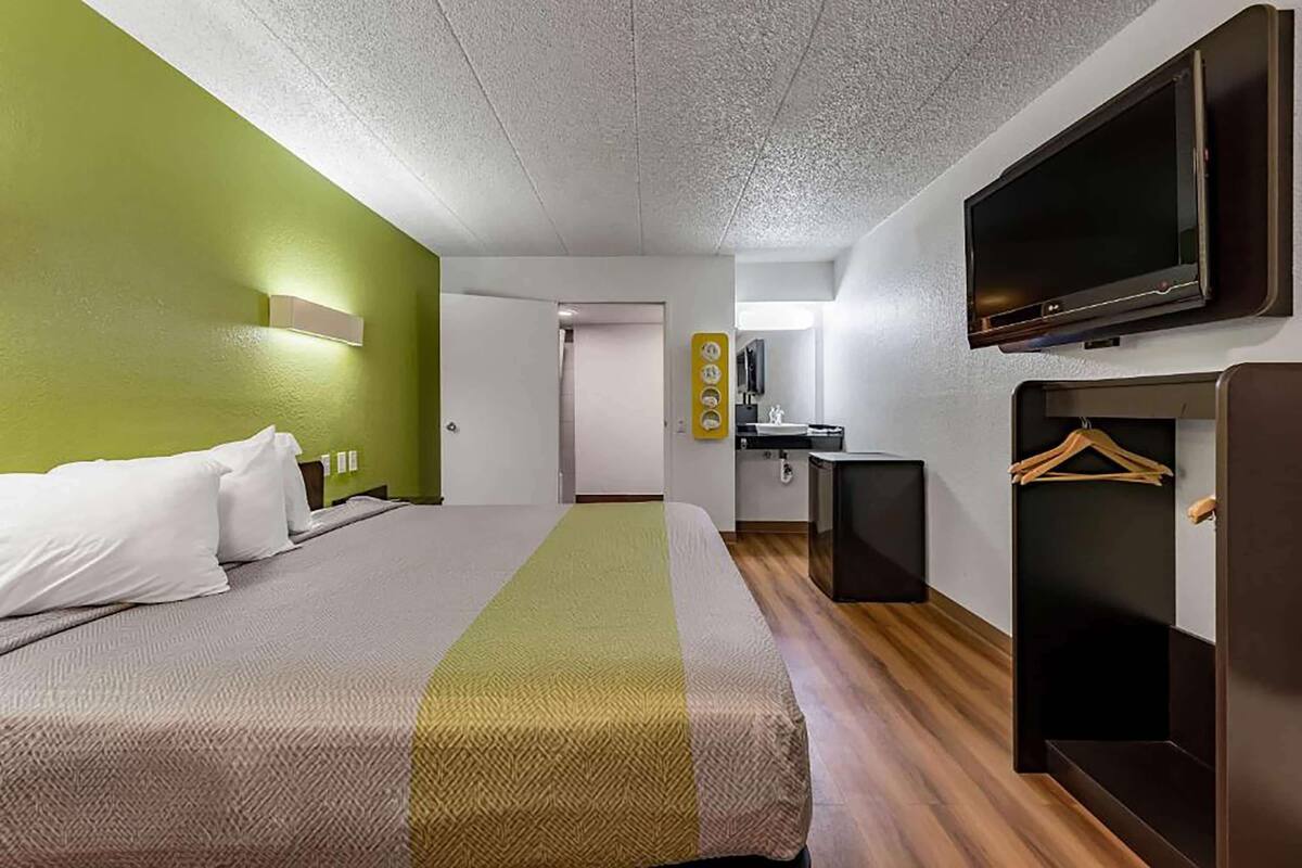 A hotel room with a bed, a TV, a small kitchenette, and a coat rack.