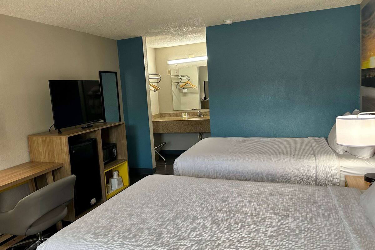 A hotel room with two beds, a desk with a television, a mirror, and a bathroom with a sink and towel rack.