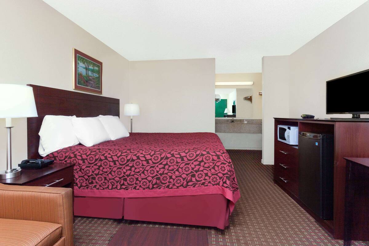 A hotel room with a bed, a desk, a chair, a television, and a microwave.