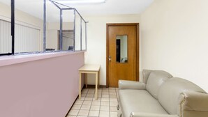 A room with a beige sofa, a small table, a wooden door, and a window with a metal frame. - Days Inn by Wyndham Columbia NE Fort Jackson (Columbia)