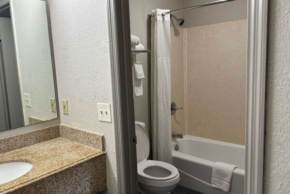 A bathroom with a granite countertop sink, a white toilet, a bathtub, and a shower curtain.
