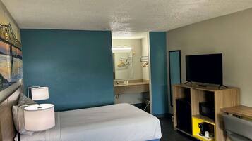 A hotel room with a bed, a desk, a TV, a mirror, and a bathroom visible through an open door.