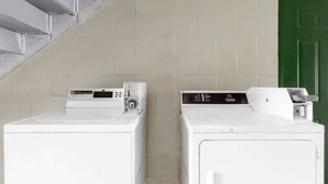 Two white front-loading washers in a laundry room with a beige tiled wall and a green door. - Days Inn by Wyndham Columbia NE Fort Jackson (Columbia)