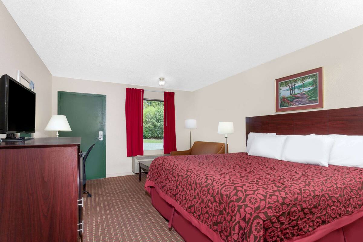 A hotel room with a large bed, a desk with a chair, a television, and a painting on the wall.