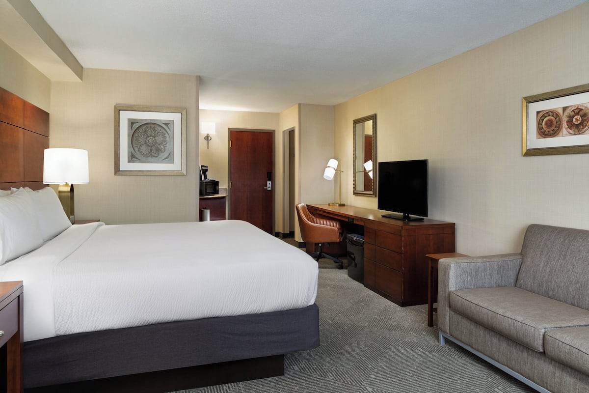 A hotel room with a large bed, a desk with a chair, a television, and a sofa.