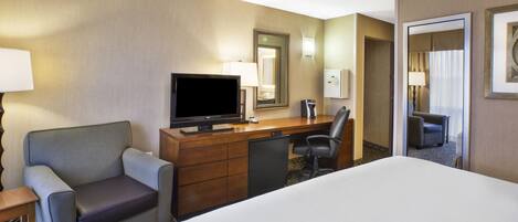 A hotel room with a bed, a desk with a television, a chair, a lamp, and a mirror.