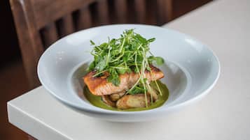 A white plate with a piece of salmon, potatoes, and greens on a white table.