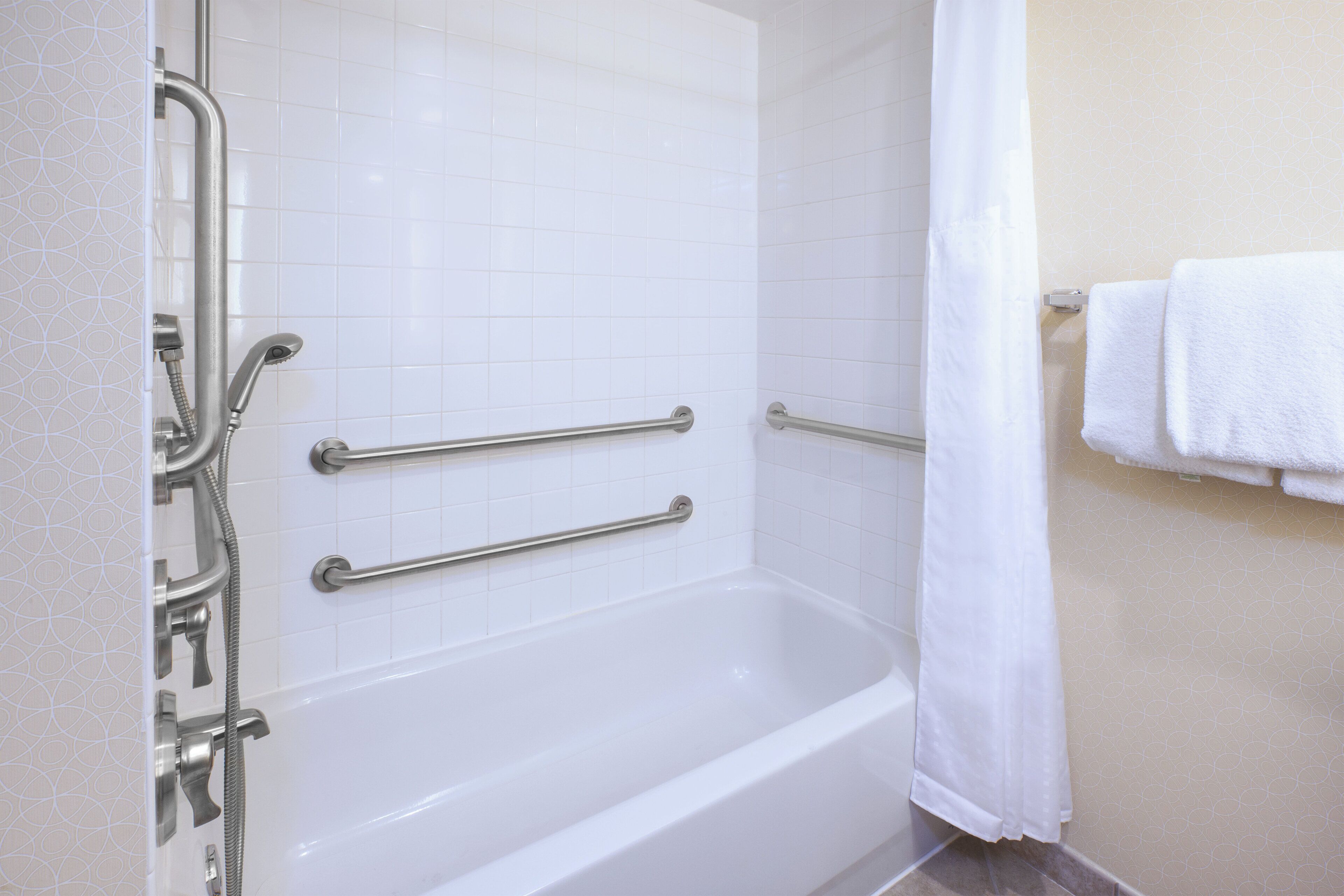 Una vasca da bagno bianca con maniglie di sostegno, un soffione doccia e un portasci con un asciugamano.