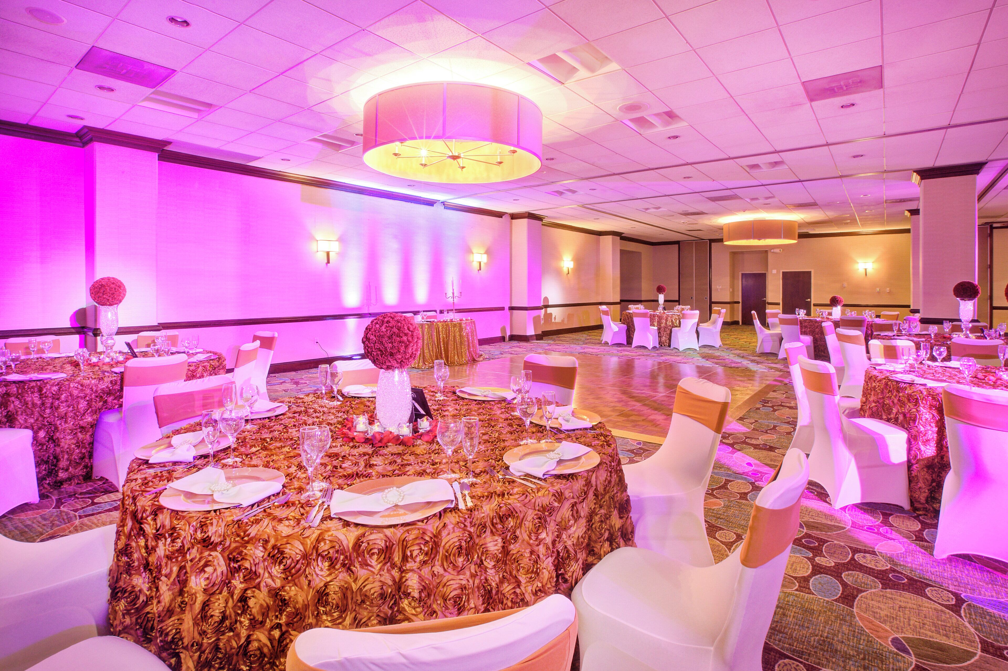 Un salón de banquetes con mesas redondas, sillas blancas y una araña de cristal.