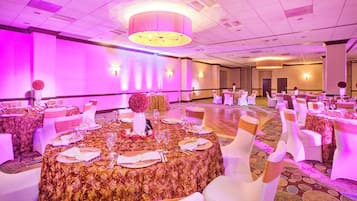 Un salón de banquetes con mesas redondas, sillas blancas y una araña de cristal.