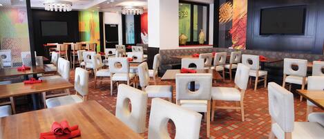 Un restaurante con varias mesas y sillas, una alfombra estampada y una pantalla grande en la pared.