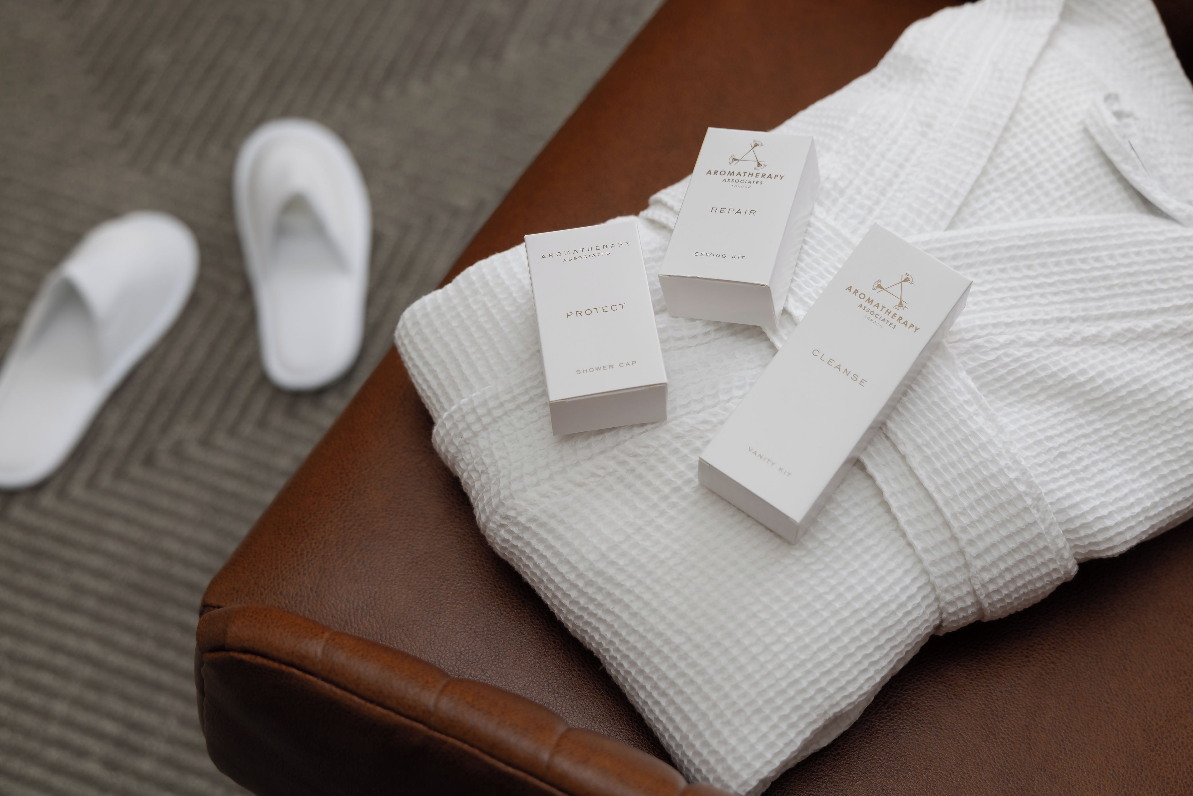 A brown leather bench with white slippers and four white boxes labeled with different aromatherapy products.