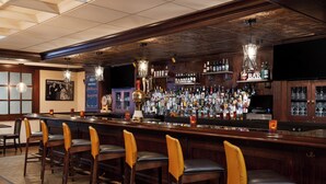 Zona de bar con mostrador de madera, varias botellas de licor y taburetes.