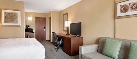 Una habitación de hotel con cama, escritorio con computadora y televisor, sofá y microondas.