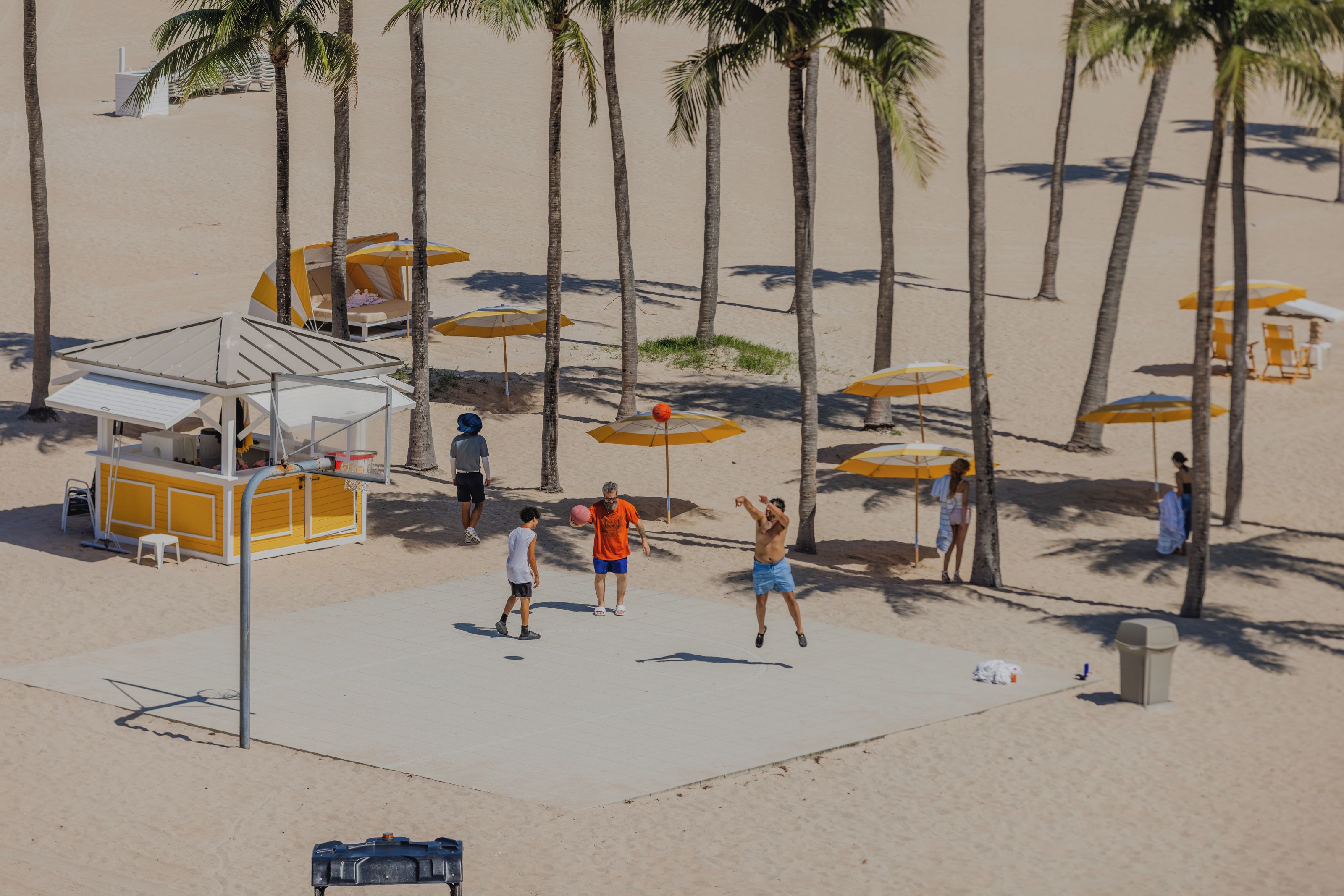 A beach with palm trees, beach umbrellas, and a small kiosk.