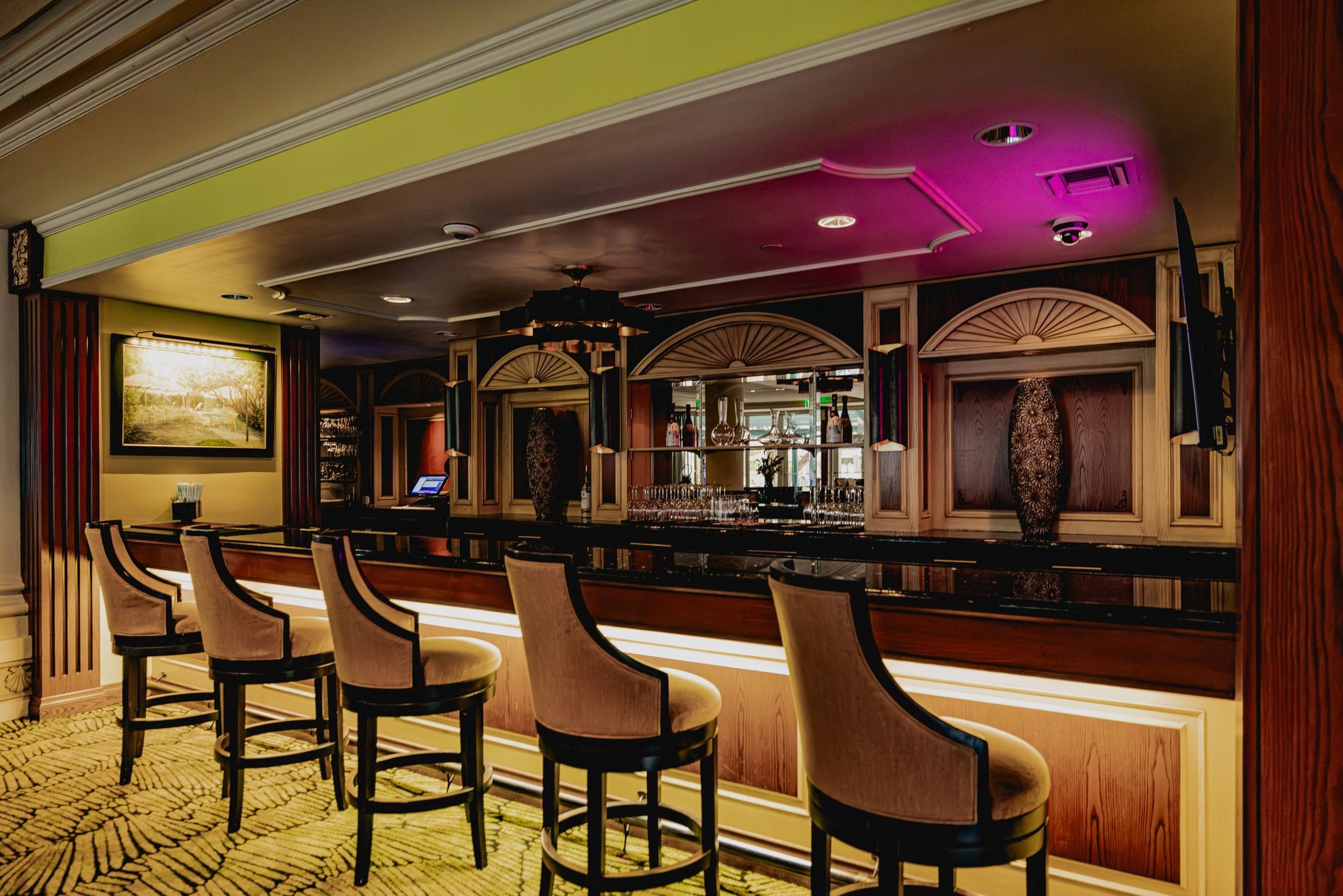 A bar area with multiple stools, a bar counter, and a large mirror.