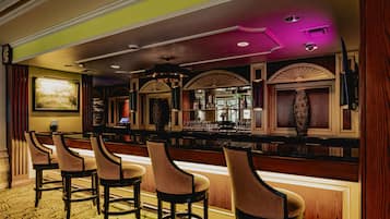 A bar area with multiple stools, a bar counter, and a large mirror.