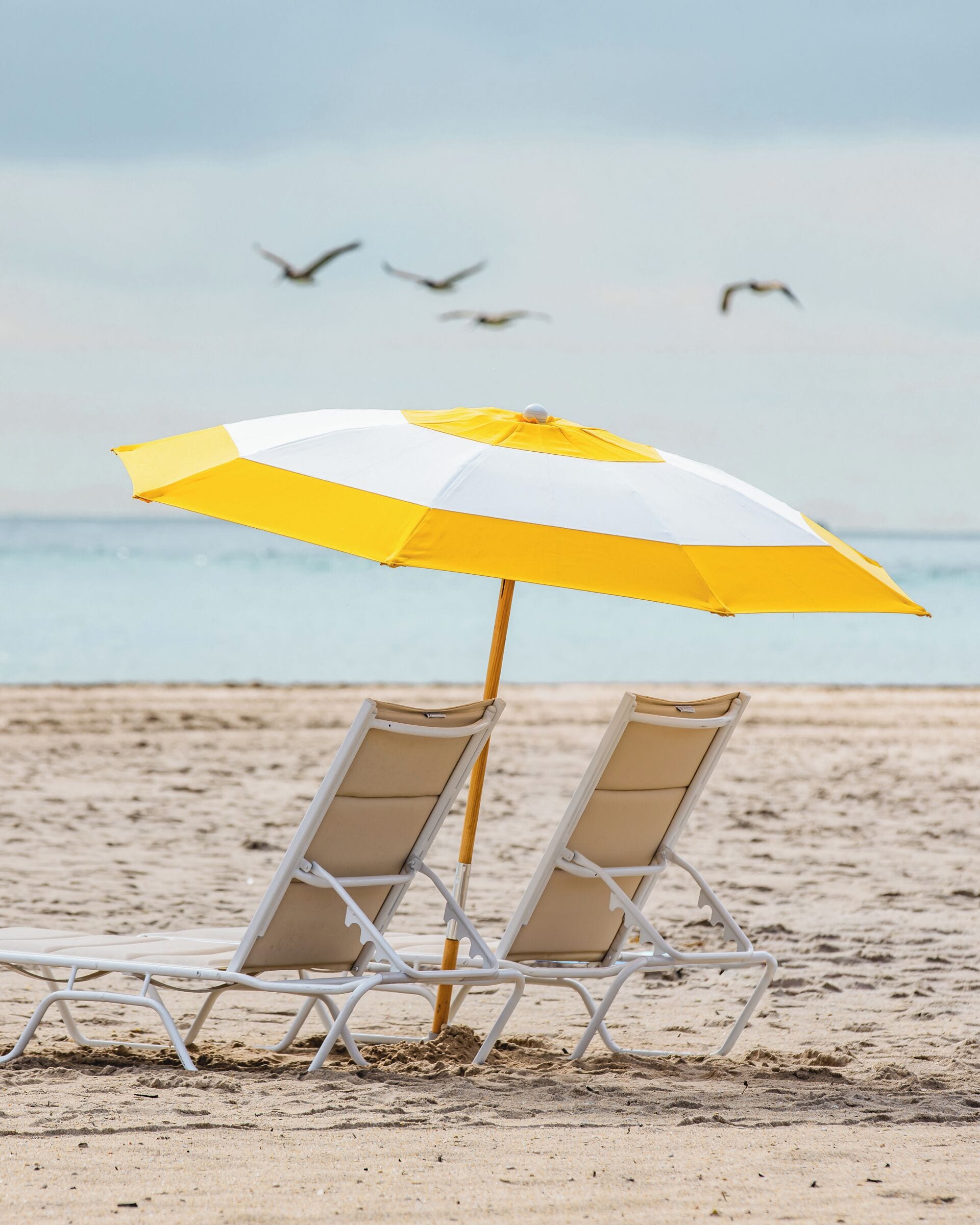 Une scène de plage avec deux chaises longues blanches et un parasol jaune et blanc.