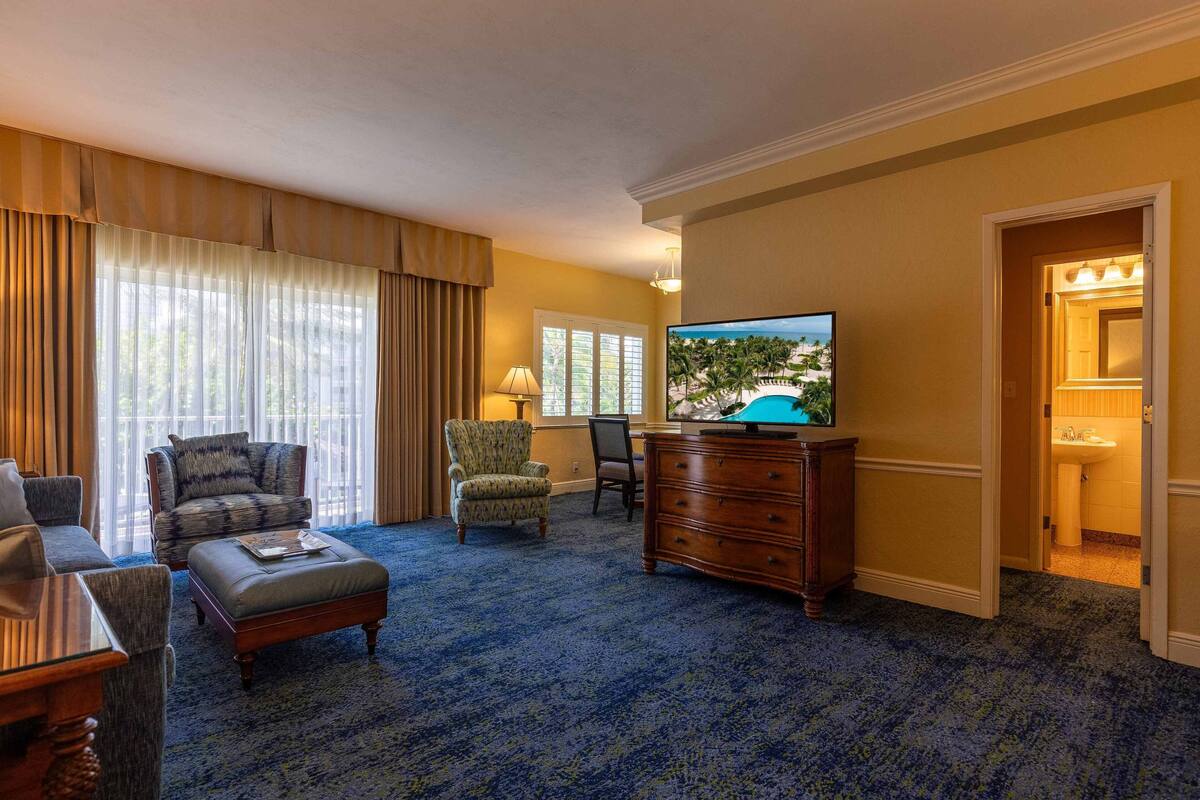 A hotel room with a large window, a television, a sofa, a chair, a desk, and a dresser.