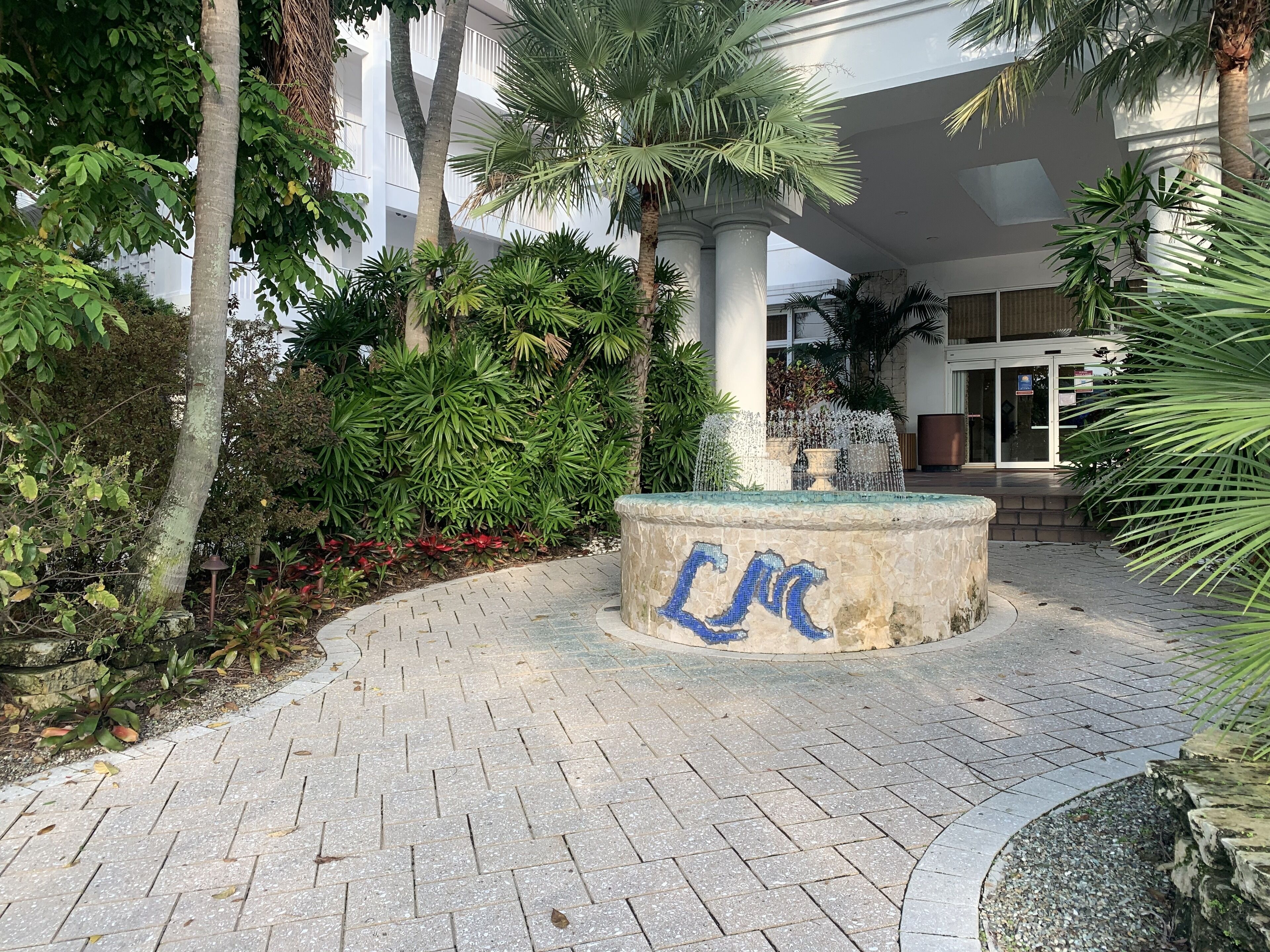 A courtyard with a fountain, surrounded by lush greenery and palm trees.