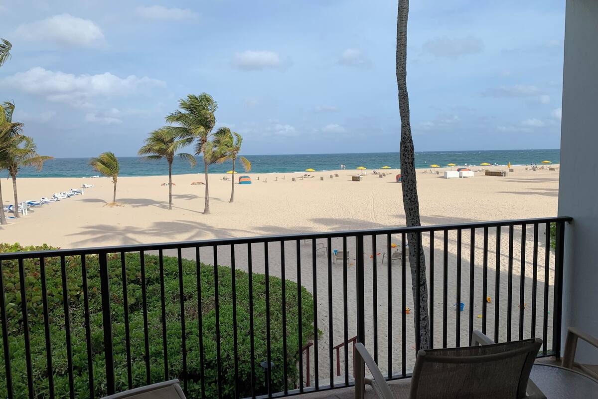A balcony with a view of a beach, palm trees, and a clear sky.