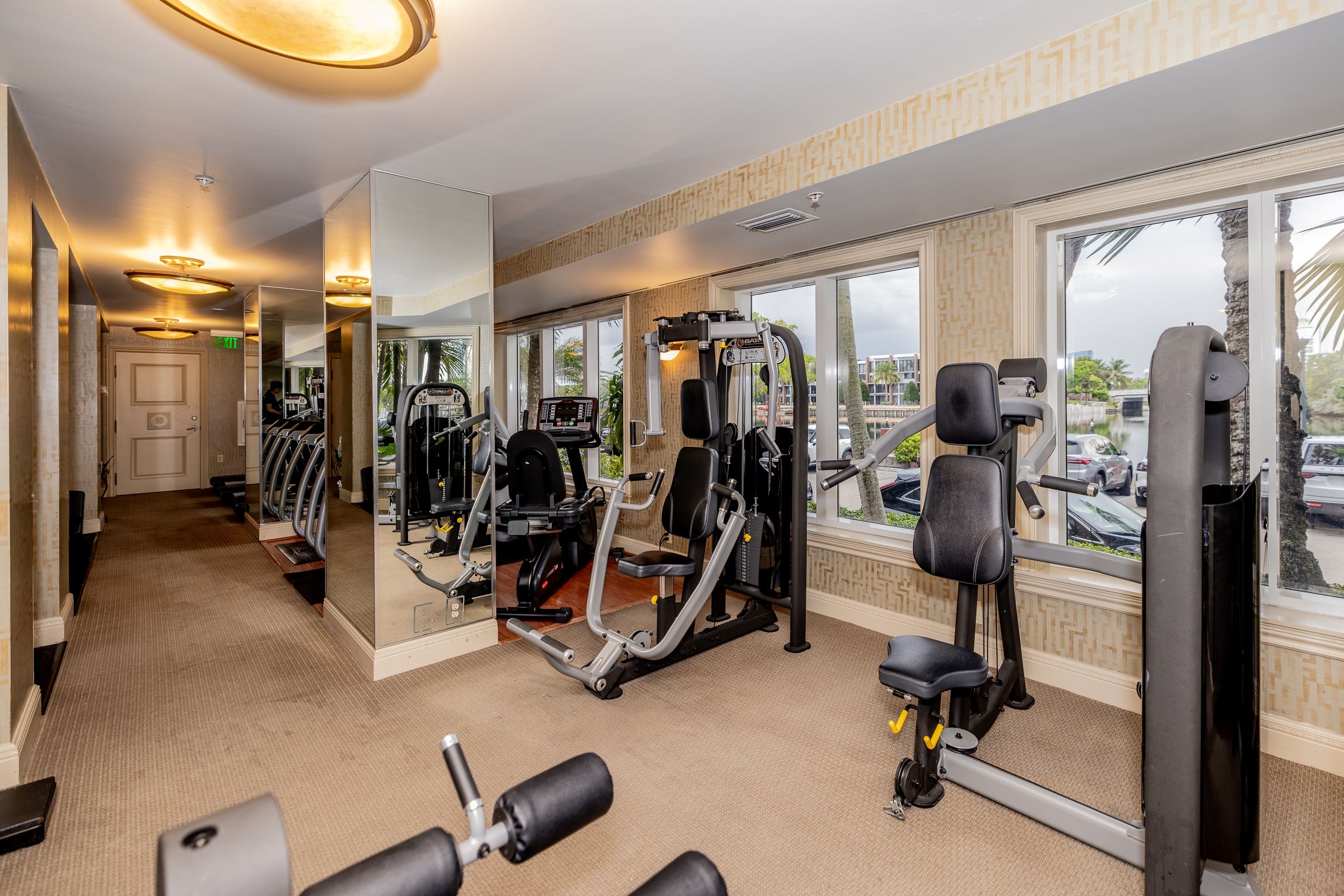 Een sportschool met diverse fitnessapparatuur, grote ramen en een vloerbedekking.