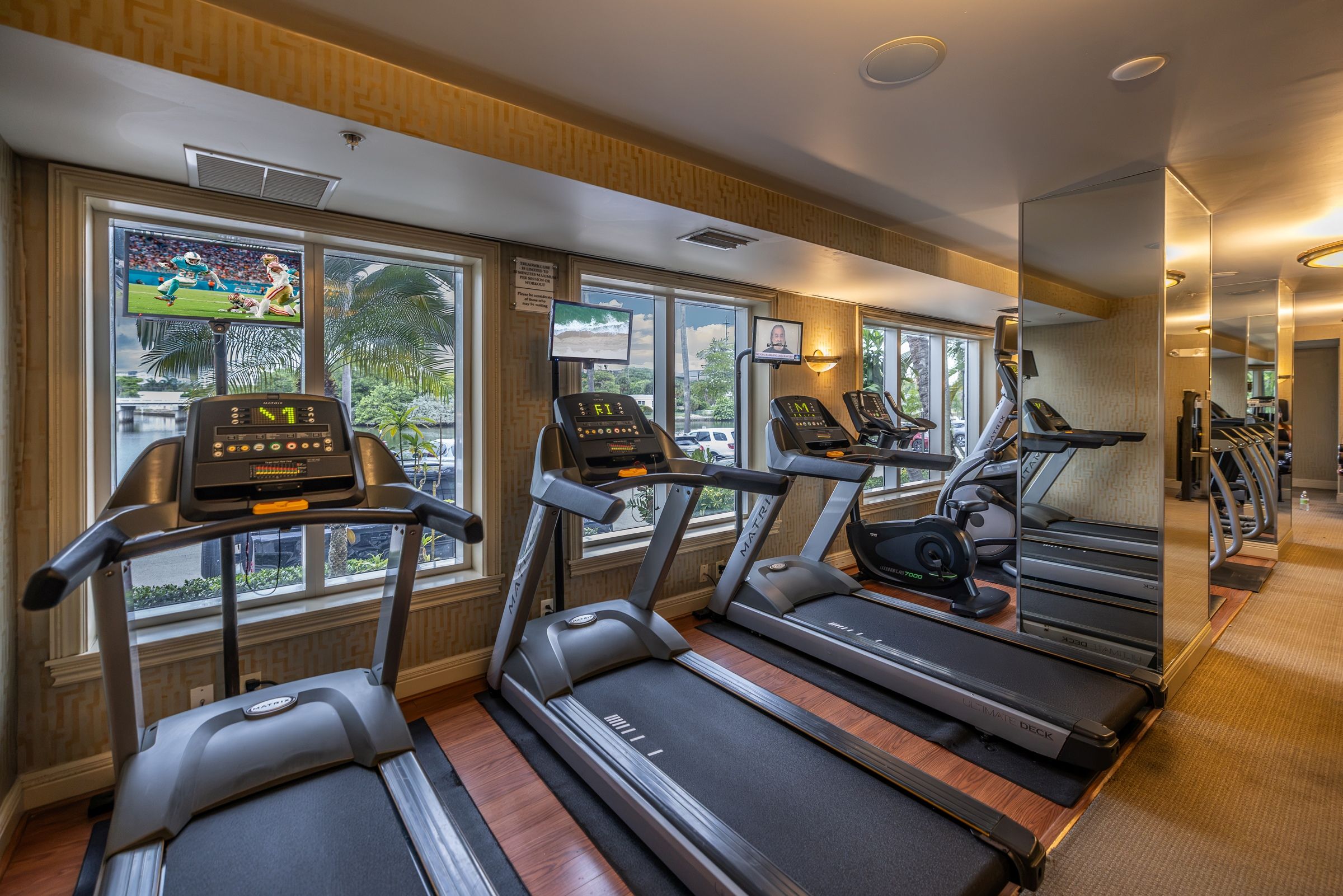 A gym with treadmills, exercise bikes, and a mirrored wall.