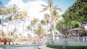 A pool area with lounge chairs, umbrellas, and palm trees.