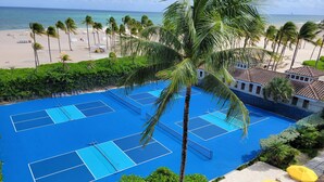 A blue tennis court with a pool, surrounded by palm trees and beach chairs. - Lago Mar Beach Resort & Club (Fort Lauderdale)