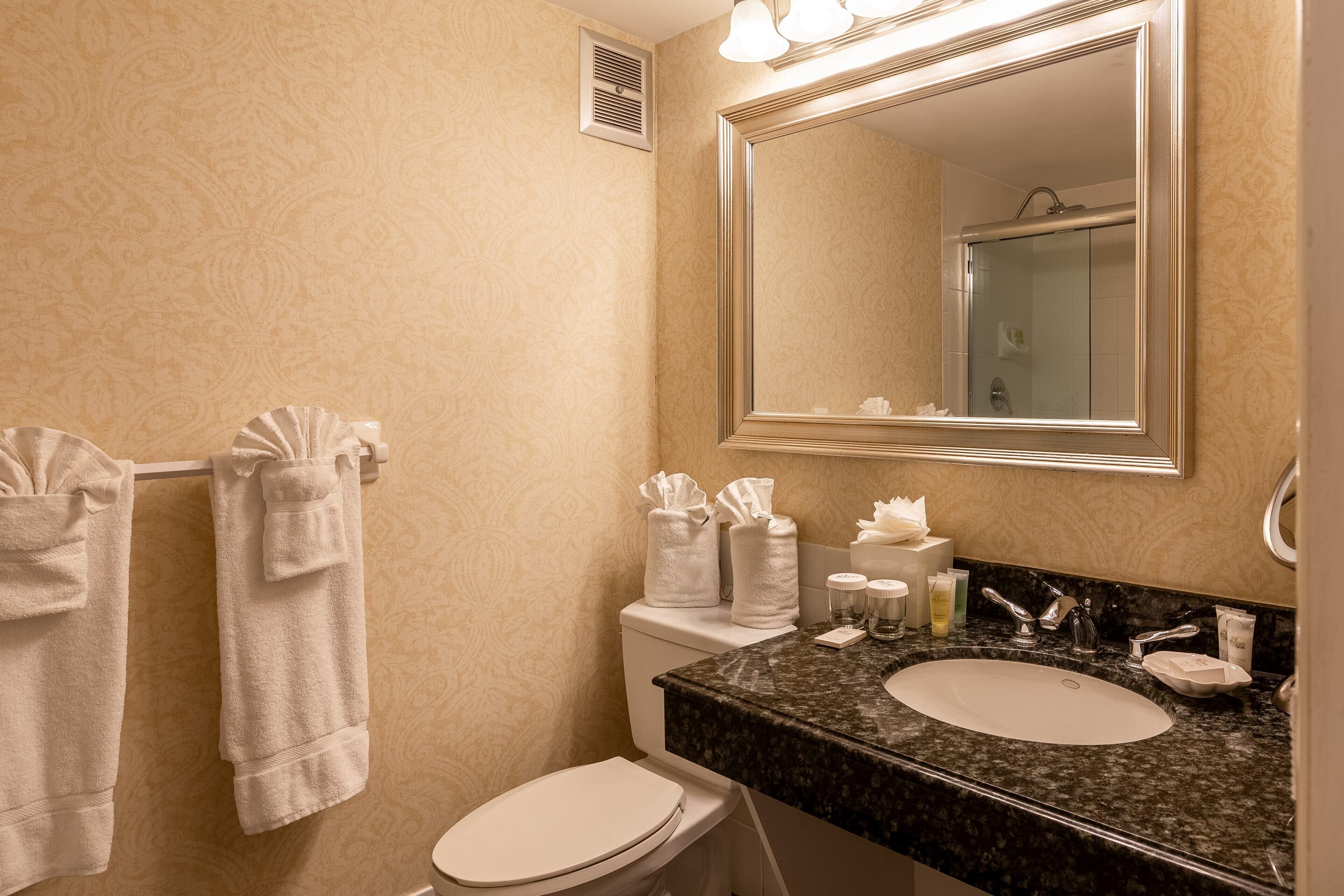 A bathroom with a toilet, sink, and mirror. There are towels hanging on a rack, and toiletries on the sink counter.