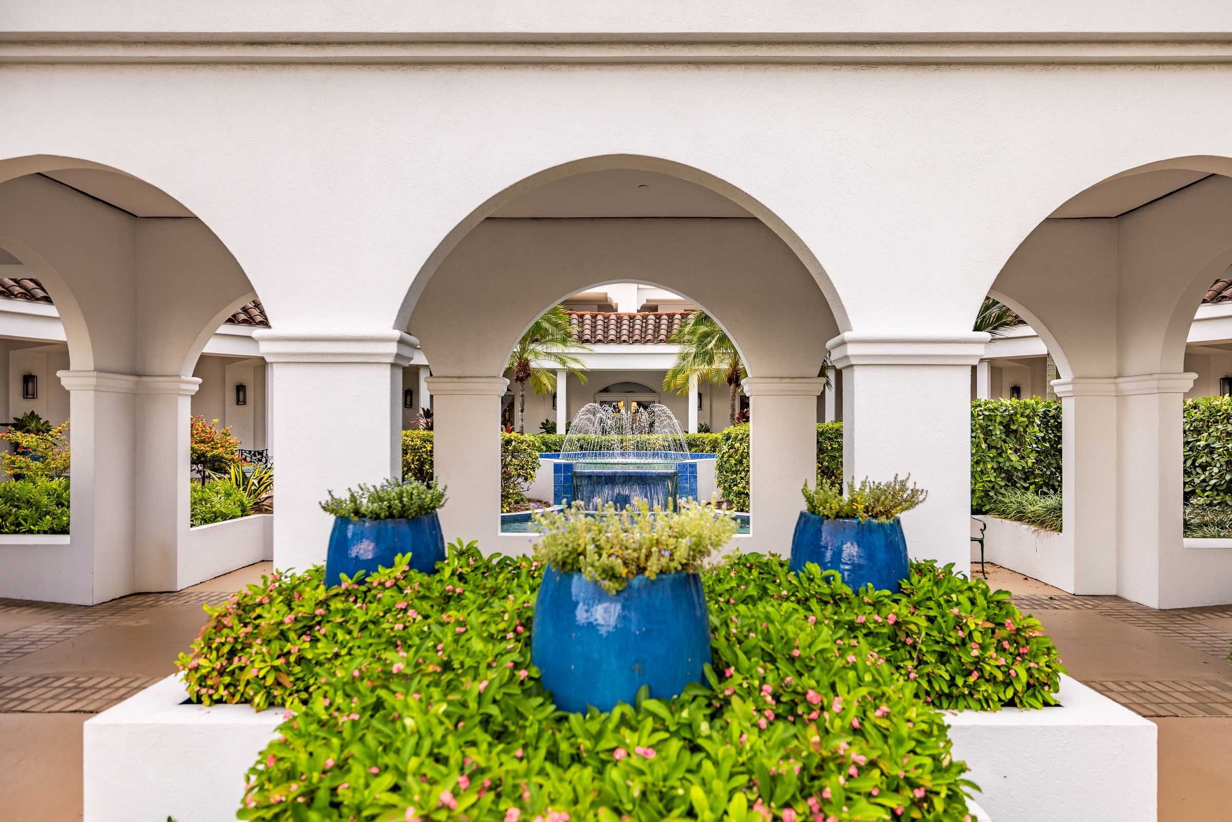 Un patio con una fuente central, rodeado de columnas blancas y macetas azules con plantas.