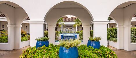 Un patio con una fuente central, rodeado de columnas blancas y macetas azules con plantas.