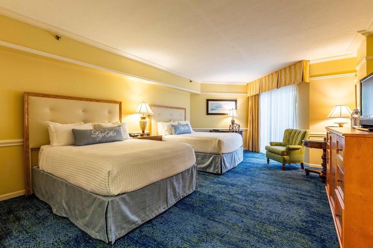 A hotel room with two beds, a desk, a chair, and a dresser.